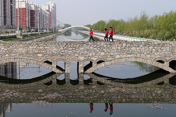 Residents walk across a bridge near a residential area in Anxin county in Xiongan New Area on Wednesday. All housing sales in the new area have been banned.Wang Zhuangfei / China Daily