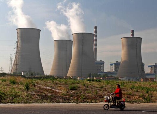 A woman passes a thermal power plant of China Huaneng Group Corp in Huai'an, Jiangsu province. By the end of this year, all coal-fired power plants of the group will be equipped with desulfurization and dust removal equipment. CHINA DAILY