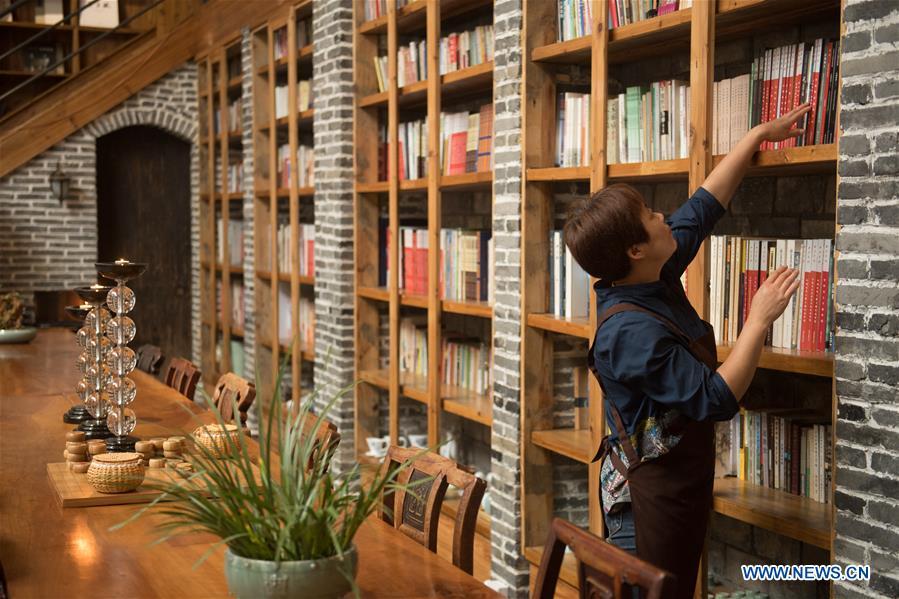 Villager Yao Wenzhen arranges books at the library in a hostel in Moganshan Town in Deqing County, east China\'s Zhejiang Province, May 29, 2018. The owner of the hostel Zhu Jindong, who worked in publishing, founded the hostel in 2015. The library collecting about 20,000 books in the hostel made it famous and attracted many tourists. (Xinhua/Weng Xinyang)