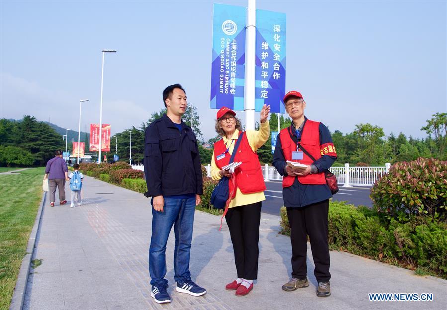 Jiang Shifa (R) and his wife Lian Shifang, volunteers for the Shanghai Cooperation Organization (SCO) Qingdao Summit, guide a tourist in Wendeng Road in Qingdao, east China\'s Shandong Province, June 5, 2018. Jiang, 74 years old and his wife, 72 years old, have been volunteers for over ten years after retired from work. The couple feel thrilled to be volunteers for the upcoming SCO Qingdao Summit ten years after they served as volunteers for the Beijing 2008 Olympic Games Sailing event in Qingdao. (Xinhua/Jiang Kehong)