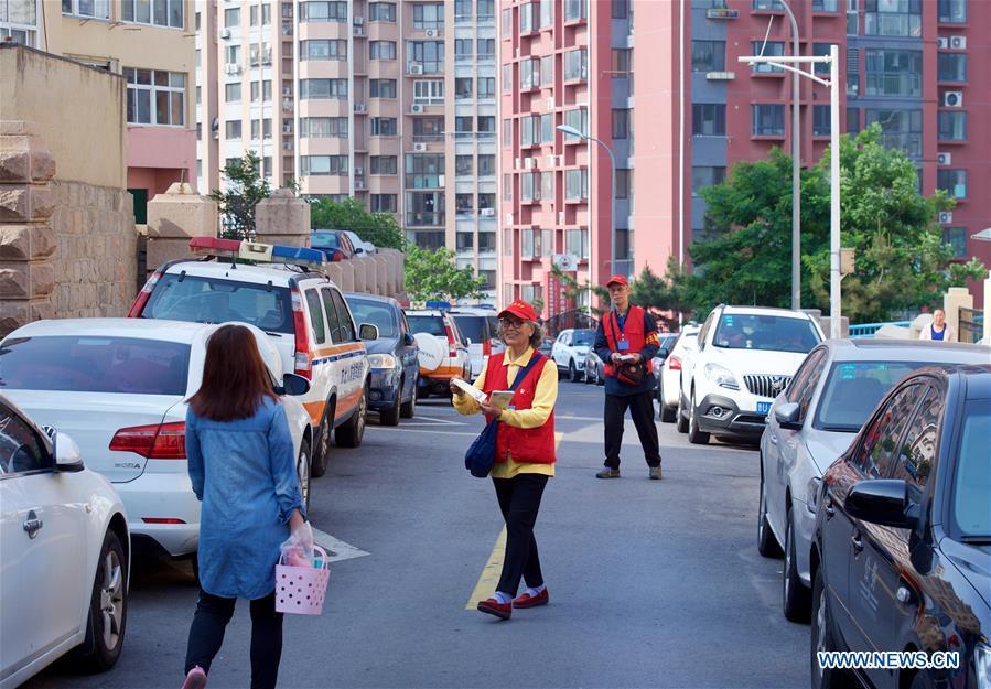 Jiang Shifa (R) and his wife Lian Shifang, volunteers for the Shanghai Cooperation Organization (SCO) Qingdao Summit, give out handbooks at Mingxialu Community in Qingdao, east China\'s Shandong Province, June 5, 2018. Jiang, 74 years old and his wife, 72 years old, have been volunteers for over ten years after retired from work. The couple feel thrilled to be volunteers for the upcoming SCO Qingdao Summit ten years after they served as volunteers for the Beijing 2008 Olympic Games Sailing event in Qingdao. (Xinhua/Jiang Kehong)