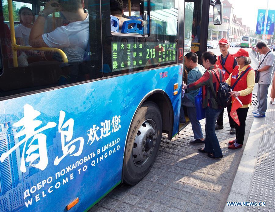 Jiang Shifa (3rd R) and his wife Lian Shifang (2nd R), volunteers for the Shanghai Cooperation Organization (SCO) Qingdao Summit, guide passengers at a bus stop in Qingdao, east China\'s Shandong Province, June 5, 2018. Jiang, 74 years old and his wife, 72 years old, have been volunteers for over ten years after retired from work. The couple feel thrilled to be volunteers for the upcoming SCO Qingdao Summit ten years after they served as volunteers for the Beijing 2008 Olympic Games Sailing event in Qingdao. (Xinhua/Jiang Kehong)