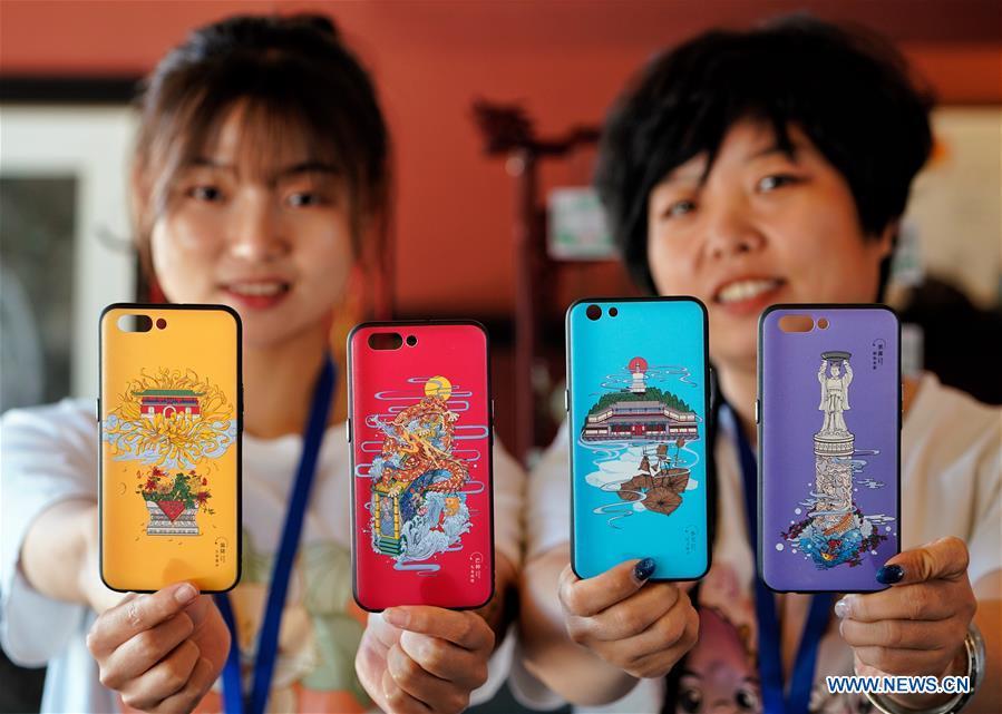Staff members show smartphone cases with creative designs based on China\'s traditional 24 solar terms at a souvenir shop in Beihai Park, Beijing, capital of China, June 20, 2018. The 24 solar terms are a list of terms central to a calendar created in ancient China. Based on the movement of the sun, the calendar divides the year into 24 segments to guide farming over the four seasons. (Xinhua/Xing Guangli)