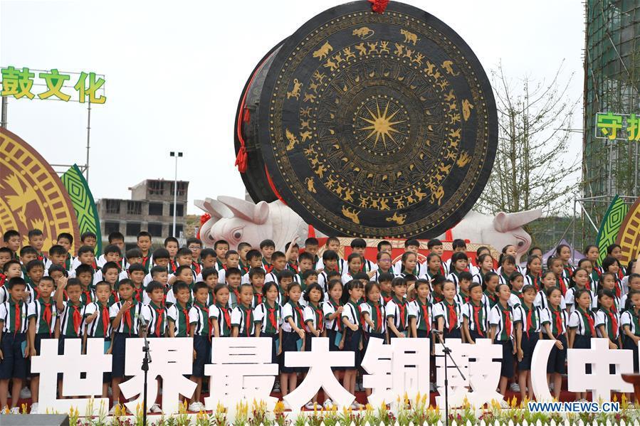 People celebrate beside a gigantic bronze drum in Huanjiang Maonan Autonomous County, south China\'s Guangxi Zhuang Autonomous Region, June 29, 2018. The drum measures 6.68 meters in diameter and weighs 50 tons. It was recognized as the largest bronze drum by Guinness World Records. (Xinhua/Zhou Hua)