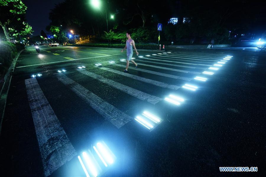 A man walks on the lighted pedestrian crossing on Xixi Road in Hangzhou, capital of east China\'s Zhejiang Province, July 2, 2018. Lamps installed along the pedestrian crossing light up at night, giving directions to pedestrians and vehicles. (Xinhua/Long Wei)