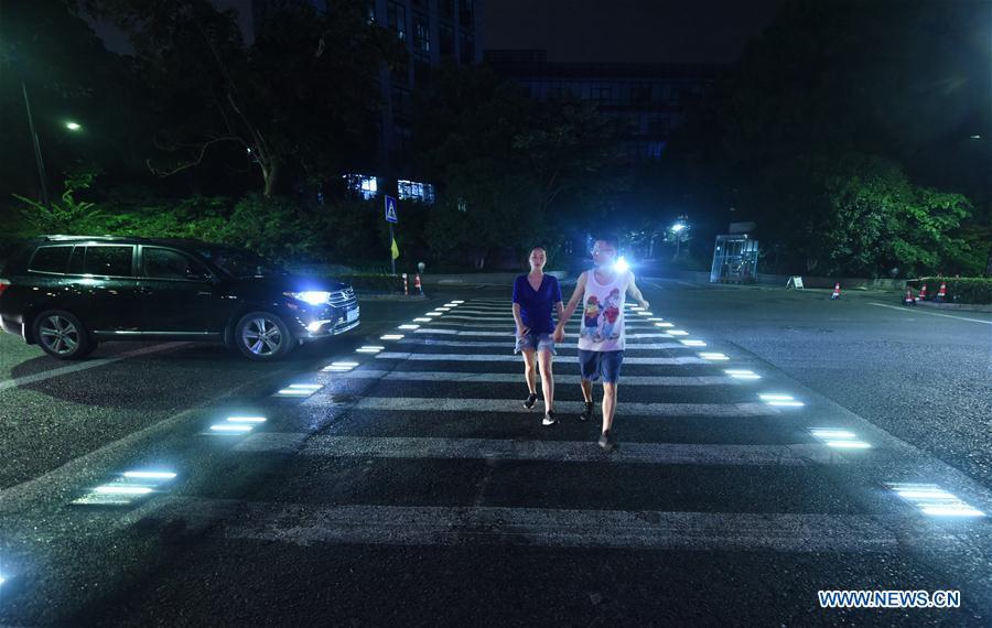 People walk on the lighted pedestrian crossing on Xixi Road in Hangzhou, capital of east China\'s Zhejiang Province, July 2, 2018. Lamps installed along the pedestrian crossing light up at night, giving directions to pedestrians and vehicles. (Xinhua/Long Wei)