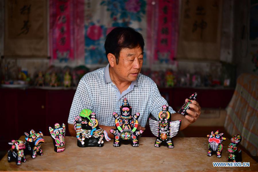 Local handicraftsman Ren Guohe displays clay statuettes in Jinzhuang Village of Huaiyang County, central China\'s Henan Province, July 9, 2018. Originated from ancient sacrificial ceremonies, the hand-made clay statuette \
