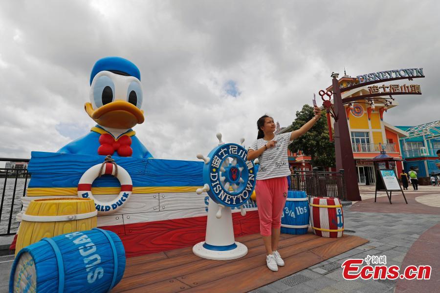 A visitor takes a selfie with an 11-meter-tall rubber Donald Duck in Wishing Star Lake at the Shanghai Disney Resort, July 12, 2018. (Photo/China News Service)