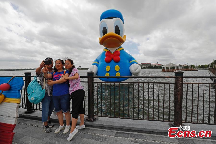 Visitors pose for photos with an 11-meter-tall Donald Duck in Wishing Star Lake at the Shanghai Disney Resort, July 12, 2018. (Photo/China News Service)