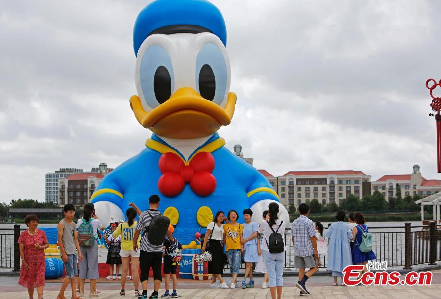 Visitors pose for photos with an 11-meter-tall Donald Duck in Wishing Star Lake at the Shanghai Disney Resort, July 12, 2018. (Photo/China News Service)