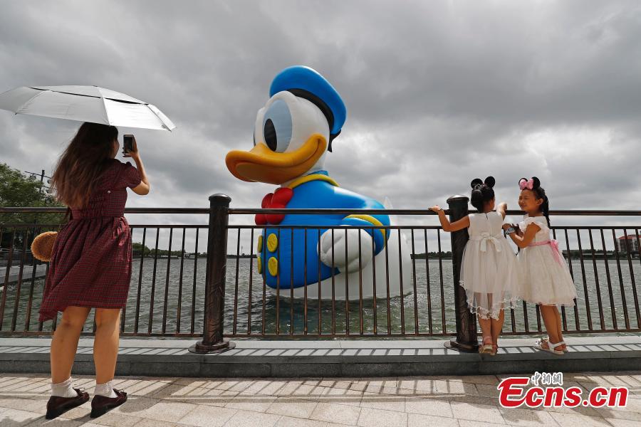 Visitors pose for photos with an 11-meter-tall Donald Duck in Wishing Star Lake at the Shanghai Disney Resort, July 12, 2018. (Photo/China News Service)