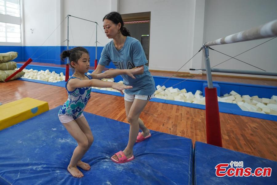 Instructor Wei Hong trains a student at the Amateur Children\'s Gymnastics Training School in Rongjiang County, Southwest China’s Guizhou Province, July 16, 2018. There are 60 children taking part in gymnastics training at the school during their spare time. Since 1972, the county has sent 21 athletes to the provincial gymnastics and gymnastics trampoline teams, among whom six later became national team members. The county is home to Liu Rongbing, who won a gold medal for the men\'s team in the 2014 World Artistic Gymnastics Championships. (Photo: China News Service/He Junyi)