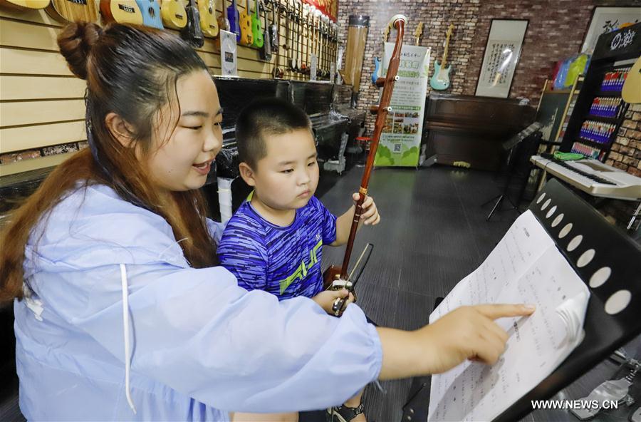 A student learns to play erhu, a Chinese two-stringed musical instrument, under the guidance of his teacher in Zunhua City, north China\'s Hebei Province, July 18, 2018. Chinese students have entered their summer vacation, during which many of them chose to spend the vacation by developing their hobbies. (Xinhua/Liu Mancang)