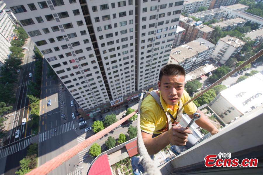 A man, attached to a rope, installs air-conditioning equipment on the outside of a tall building in Taiyuan City, North China’s Shanxi Province, July 20, 2018. (Photo: China News Service/Zhang Yun)