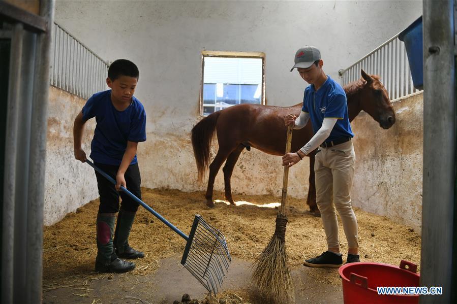 Huang Wanpeng (R), a student of Sunshine Riding School, cleans up the school stable together with one of his juniors in Yihuang County of Fuzhou, east China\'s Jiangxi Province, July 25, 2018. Equestrianism had never been heard of in Yihuang, an agricultural county in east China\'s Jiangxi Province, until Sunshine Riding School began recruiting rural teenagers in 2015. So far, most of the 90 students are working or aspiring to work in horse riding clubs in China\'s largest cities such as Beijing, Shanghai and Hangzhou. (Xinhua/Zhou Mi)