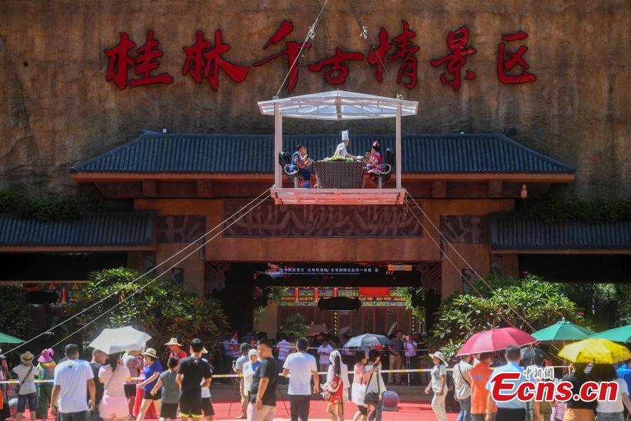 Participants face the challenge of eating rice noodles in a transparent room, hoisted 50 meters off the ground, near a giant statue at a scenic spot in Guilin City, South China’s Guangxi Zhuang Autonomous Region, July 29, 2018. Scared of the height, the participants gave up on the dare when the room was just ten meters off the ground. (Photo: China News Service/Chen Chen)