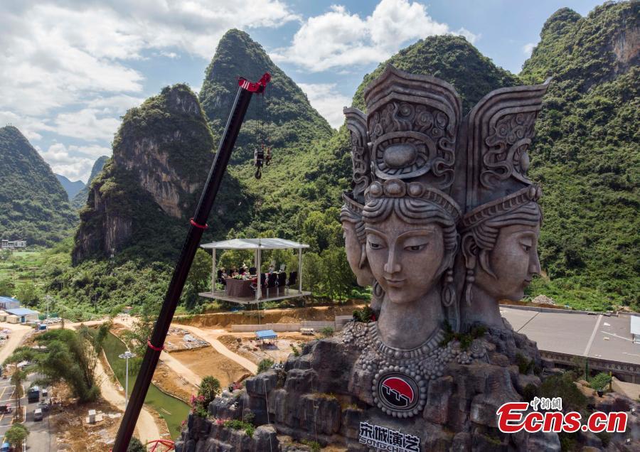 Participants face the challenge of eating rice noodles in a transparent room, hoisted 50 meters off the ground, near a giant statue at a scenic spot in Guilin City, South China’s Guangxi Zhuang Autonomous Region, July 29, 2018. Scared of the height, the participants gave up on the dare when the room was just ten meters off the ground. (Photo: China News Service/Chen Chen)