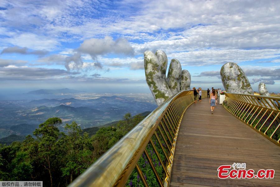 In this photograph taken on July 31, 2018, visitors walk along the 150-meter long Cau Vang \'Golden Bridge\' in the Ba Na Hills near Danang. Nestled in the forested hills of central Vietnam two giant concrete hands emerge from the trees, holding up a glimmering golden bridge crowded with gleeful visitors taking selfies at the country\'s latest eccentric tourist draw. Suspended 1400 meters above sea level, the bridge combines eight sections and stretches 150 meters long. (Photo/VCG)