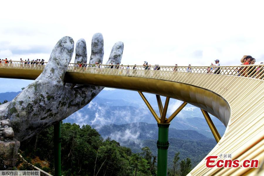 In this photograph taken on July 31, 2018, visitors walk along the 150-meter long Cau Vang \'Golden Bridge\' in the Ba Na Hills near Danang. Nestled in the forested hills of central Vietnam two giant concrete hands emerge from the trees, holding up a glimmering golden bridge crowded with gleeful visitors taking selfies at the country\'s latest eccentric tourist draw. Suspended 1400 meters above sea level, the bridge combines eight sections and stretches 150 meters long. (Photo/VCG)