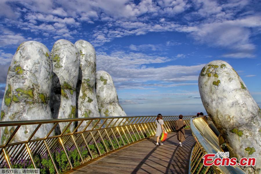 In this photograph taken on July 31, 2018, visitors walk along the 150-meter long Cau Vang \'Golden Bridge\' in the Ba Na Hills near Danang. Nestled in the forested hills of central Vietnam two giant concrete hands emerge from the trees, holding up a glimmering golden bridge crowded with gleeful visitors taking selfies at the country\'s latest eccentric tourist draw. Suspended 1400 meters above sea level, the bridge combines eight sections and stretches 150 meters long. (Photo/VCG)