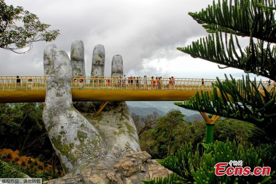 In this photograph taken on July 31, 2018, visitors walk along the 150-meter long Cau Vang \'Golden Bridge\' in the Ba Na Hills near Danang. Nestled in the forested hills of central Vietnam two giant concrete hands emerge from the trees, holding up a glimmering golden bridge crowded with gleeful visitors taking selfies at the country\'s latest eccentric tourist draw. Suspended 1400 meters above sea level, the bridge combines eight sections and stretches 150 meters long. (Photo/VCG)