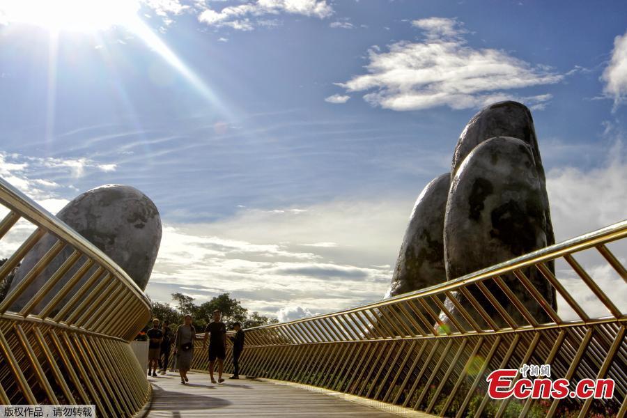 In this photograph taken on July 31, 2018, visitors walk along the 150-meter long Cau Vang \'Golden Bridge\' in the Ba Na Hills near Danang. Nestled in the forested hills of central Vietnam two giant concrete hands emerge from the trees, holding up a glimmering golden bridge crowded with gleeful visitors taking selfies at the country\'s latest eccentric tourist draw. Suspended 1400 meters above sea level, the bridge combines eight sections and stretches 150 meters long. (Photo/VCG)