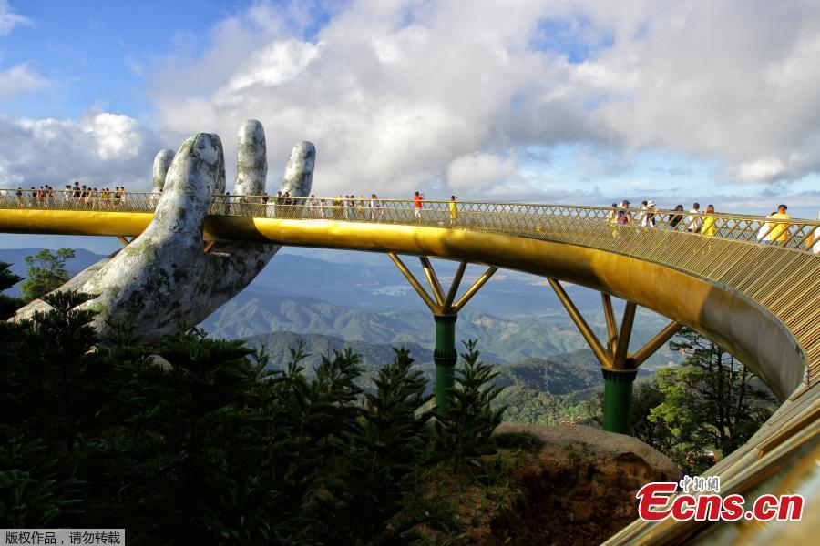 In this photograph taken on July 31, 2018, visitors walk along the 150-meter long Cau Vang \'Golden Bridge\' in the Ba Na Hills near Danang. Nestled in the forested hills of central Vietnam two giant concrete hands emerge from the trees, holding up a glimmering golden bridge crowded with gleeful visitors taking selfies at the country\'s latest eccentric tourist draw. Suspended 1400 meters above sea level, the bridge combines eight sections and stretches 150 meters long. (Photo/VCG)