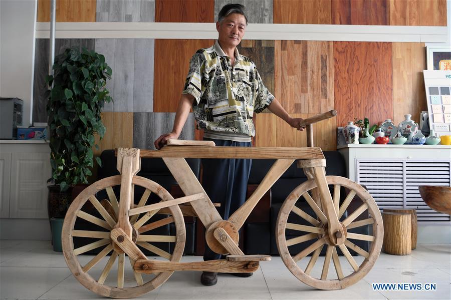 He Yong shows his wooden bicycle in Liuhu Township of Pingliang City, northwest China\'s Gansu Province, Aug. 14, 2018. The 55-year-old farmer He Yong successfully made a 1.8-meter-long and 0.98-meter-high wooden bicycle in 2017. The bike was made purely of wood, including walnut and elm. (Xinhua/Fan Peishen)