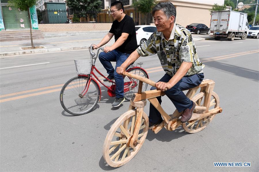 He Yong rides a wooden bicycle on a road in Pingliang City, northwest China\'s Gansu Province, Aug. 14, 2018. The 55-year-old farmer He Yong successfully made a 1.8-meter-long and 0.98-meter-high wooden bicycle in 2017. The bike was made purely of wood, including walnut and elm. (Xinhua/Fan Peishen)