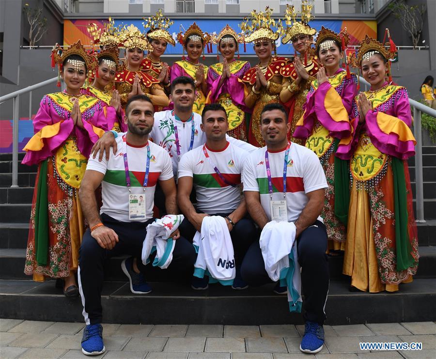 Iranian athletes pose for pictures with etiquette team members in Indonesian folk costume at the Asian Games Village ahead of the 18th Asian Games in Jakarta, Indonesia, on Aug. 16, 2018. (Xinhua/Wang Yuguo)