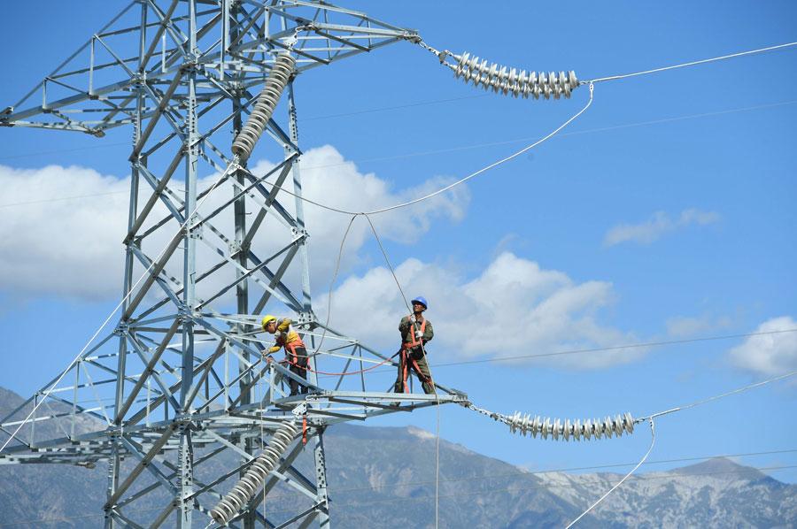 An employee connects electrical cables atop a 30-meter-high, 110 kV power transmission tower in the Tibet autonomous region. (Photo by Song Weixing/For China Daily)