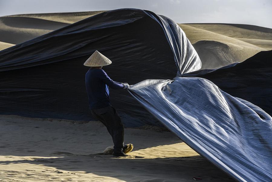 A worker covers the roadbed with woven plastic film before the arrival of a sandstorm. (Photo/Xinhua)