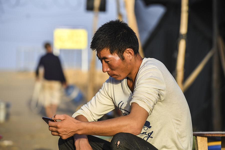 Xie Chunlong, a worker from Qinghai province, watches a TV drama on his mobile phone on a break from his work building a new road through the Taklimakan Desert in the Xinjiang Uygur autonomous region. (Photo/Xinhua)
The second, which stretches 424 km, was completed in 2007. It links the resource-rich and densely populated city of Hotan, in southern Xinjiang, with Aral, an underdeveloped city on the northern edge of the desert.
This new road will cover about 330 km and is expected to open in 2021. Hundreds of people from across the country have been recruited to construct it. After starting work in Qiemo, they have reached the desert\'s hinterland, more than 60 km away.
Li Qiushen, chief engineer of the highway project, who is also experienced in desert road construction, said he understands how difficult this project is.
\
