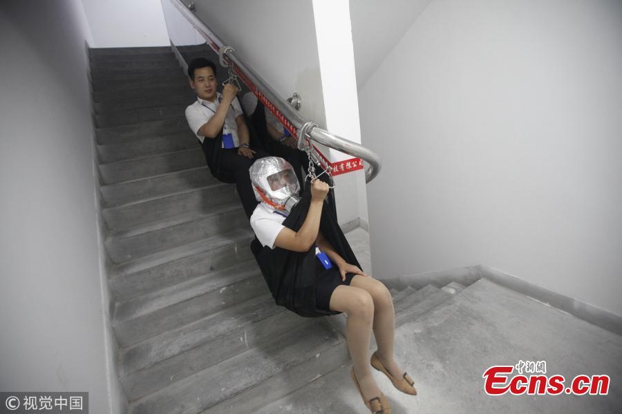 An emergency escape system designed for use in high-rise buildings was unveiled in Xi\'an, Shaanxi Province on Wednesday. If a fire breaks out, people can glide down through the stairwell at a speed of around 1 meter per second using a special railing that can bear the weight of a 100 kilogram person. The emergency exit also has respirators to protect evacuees from poisonous dust and gases. In this photo taken on Wednesday, August 22, 2018 two staff members from the developer of the system demonstrate how it is used. (Photo/VCG)