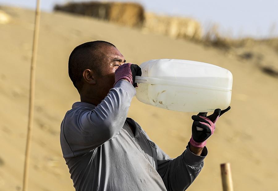 A worker drinks water during the break. (Photo/Xinhua)
This new road, however, could be his toughest project yet. Working for 10 hours a day, he makes hundreds of trips between dunes, digging up to 2,000 cubic meters of sand.
Towers of sand
More than a half of China\'s total desert area is in Xinjiang. Roads such as the one being built by Zhang and his colleagues are essential, making it easier for residents and goods to travel through these areas.
The first highway across the Taklimakan was opened to traffic in 1995 and runs north to south from Lunnan town to Minfeng county. At 522 km, it is the world\'s longest desert highway.