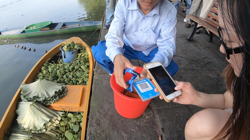 A young woman uses Alipay to buy lotus heads and leaves. (Photo/China Daily)
Ni Bing, a 26-year-old administrative worker and the only young person among the 30 standing in line that day, said the West Lake\'s unique appeal motivates him to get up early and join those who are waiting.
\