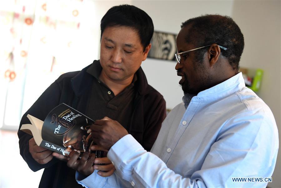 Diarra introduces an English book about the traditional Chinese medicine to his friend in Kunming, southwest China\'s Yunnan Province, Aug. 28, 2018.(Xinhua/Lin Yiguang)