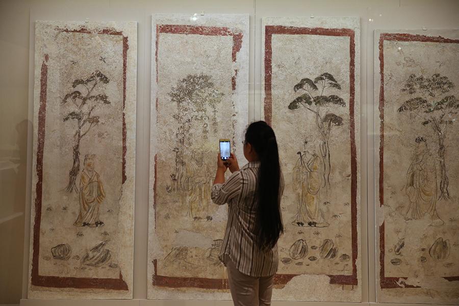 A visitor takes photos of exhibited paintings. (Photo/China Daily)