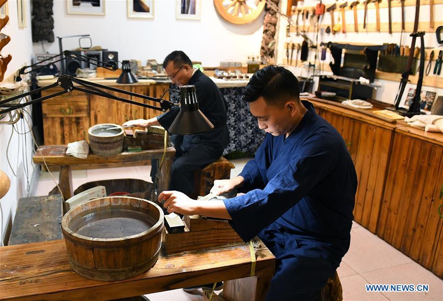 Yan Min (back) restores ancient weapons with his son in Shijiazhuang, north China\'s Hebei Province, Sept. 11, 2018. Yan Min, dedicated to ancient weapon restoration for more than 30 years, has hitherto repaired over 500 pieces of ancient weapons with his son Yan Peng. Influenced by his father, Yan Peng quit his job and embarked on restoring ancient weapons in the year of 2015. The sophisticated craftsmanship of ancient weapon restoration embodies working procedures of polishing, burnishing, grinding etc. \