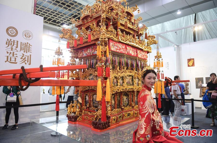 A woman wearing traditional wedding clothes poses for photo before a Ningbo Wedding Sedan Chair at the fifth China Intangible Cultural Heritage Expo in Jinan City, Shandong Province, Sept. 13, 2018. The expo was jointly organized by the Ministry of Culture and Tourism and the Shandong provincial government. More than 200 practitioners of traditional arts and craftsmanship will showcase their skills at the expo, which will include stilt-walking, embroidery by the Qiang people and straw-weaving craftworks. (Photo: China News Service/Zhang Yong)