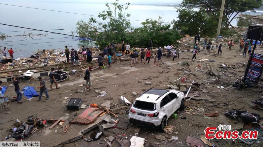 People walk past dead bodies (blue cover) a day after an earthquake and a tsunami hit Palu, on Sulawesi island on September 29, 2018. Rescuers scrambled to reach tsunami-hit central Indonesia and assess the damage after a strong quake brought down several buildings and sent locals fleeing their homes for higher ground.(Photo/Agencies)