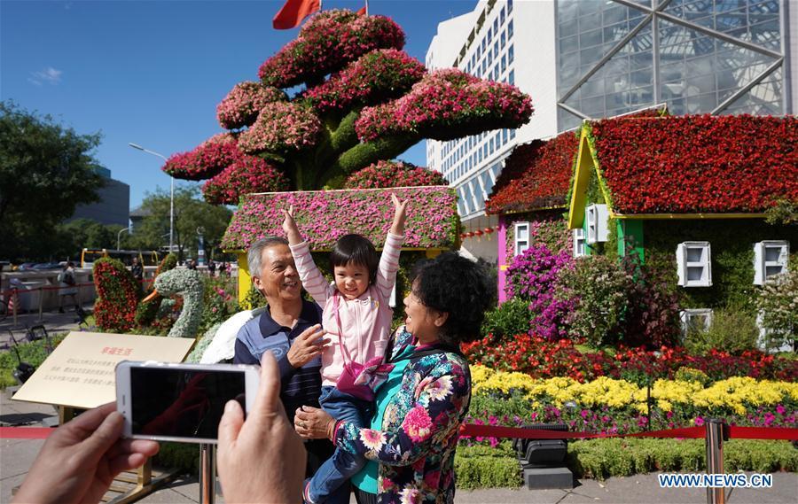 Pedestrians pose for photos with flower parterres in Beijing, capital of China, Sept. 29, 2018. Beijing is decorated with ornamental flower parterres for the upcoming China\'s National Day. (Xinhua/Ju Huanzong)