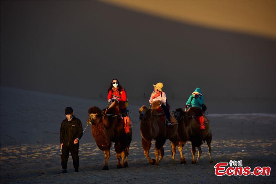 Tourists ride camels in a tour of the Mingsha Hill scenic spot in the Gobi Desert in Dunhuang City, Northwest China\'s Gansu Province, during the National Day holiday from Oct. 1 to 7. Consisting of a group of sand dunes, the Mingsha Hill, with a name that means \'singing sand\', is famous for its desert scenery and the mysterious sound made by the wind as it blows over its surface. The scenic spot attracted 307,900 tourists during the holiday, a year-on-year growth of nine percent, and achieved a tourism revenue of 330 million yuan ($47.7 million), up 10 percent on the same period last year. (Photo: China News Service/Wang Binyin)