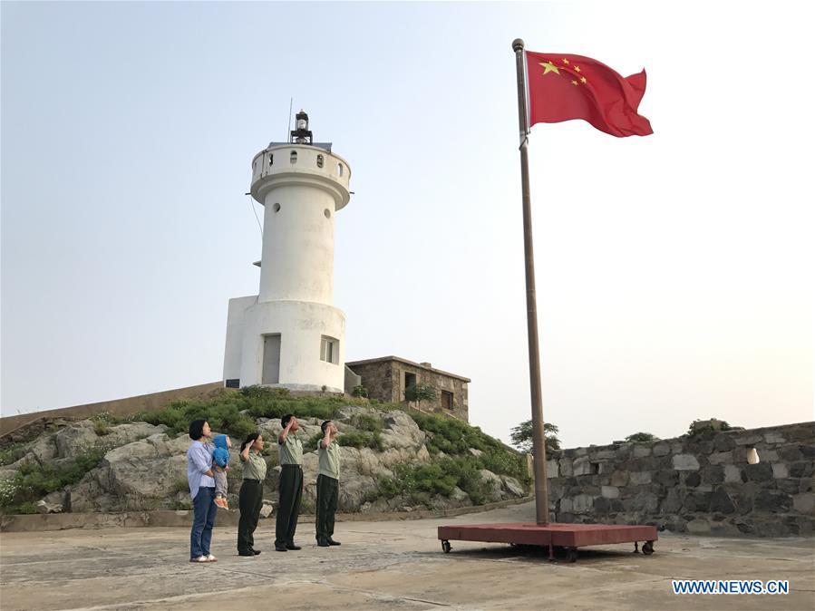 Wang Zhiguo (1st R) salutes the national flag with his family on Kaishan Island of Guanyun County, east China\'s Jiangsu Province, Sept. 12, 2017. Wang Jicai, who used to be head of the militia post on Kaishan Island in Jiangsu Province, started working on the island in the Yellow Sea with his wife in 1986. He died of sudden illness while on duty in July of 2018 at the age of 58. Wang Zhiguo, son of Wang Jicai, became a frontier defence policeman after his graduation from Nanjing University of Aeronautics and Astronautics in 2013. He had been assigned to many security tasks for major events during 5 years\' working. (Xinhua/Li Xiang)