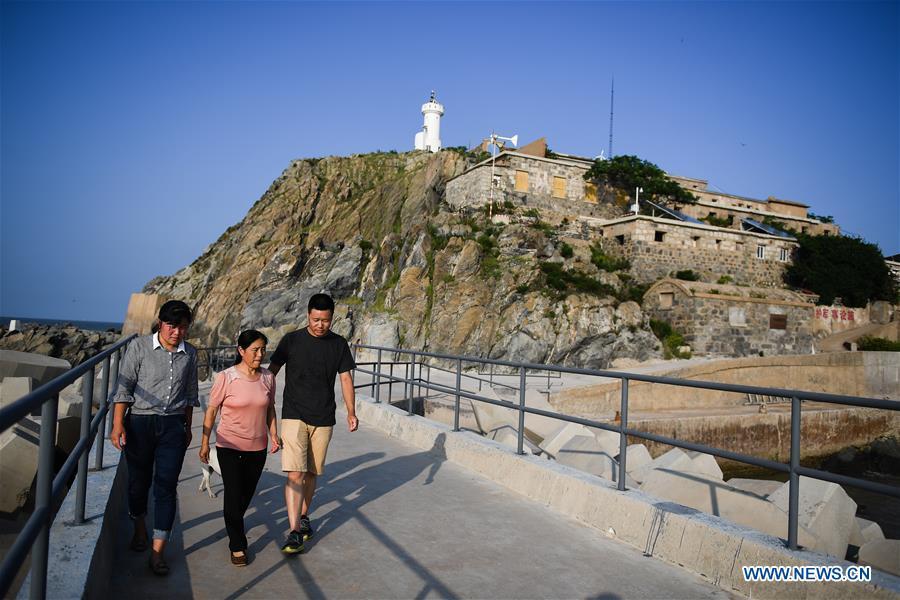 Wang Zhiguo (R) walks on a dock with his mother Wang Shihua (C) and sister Wang Su (L) on Kaishan Island of Guanyun County, east China\'s Jiangsu Province, Aug. 8, 2018. Wang Jicai, who used to be head of the militia post on Kaishan Island in Jiangsu Province, started working on the island in the Yellow Sea with his wife in 1986. He died of sudden illness while on duty in July of 2018 at the age of 58. Wang Zhiguo, son of Wang Jicai, became a frontier defence policeman after his graduation from Nanjing University of Aeronautics and Astronautics in 2013. He had been assigned to many security tasks for major events during 5 years\' working. (Xinhua/Li Xiang)