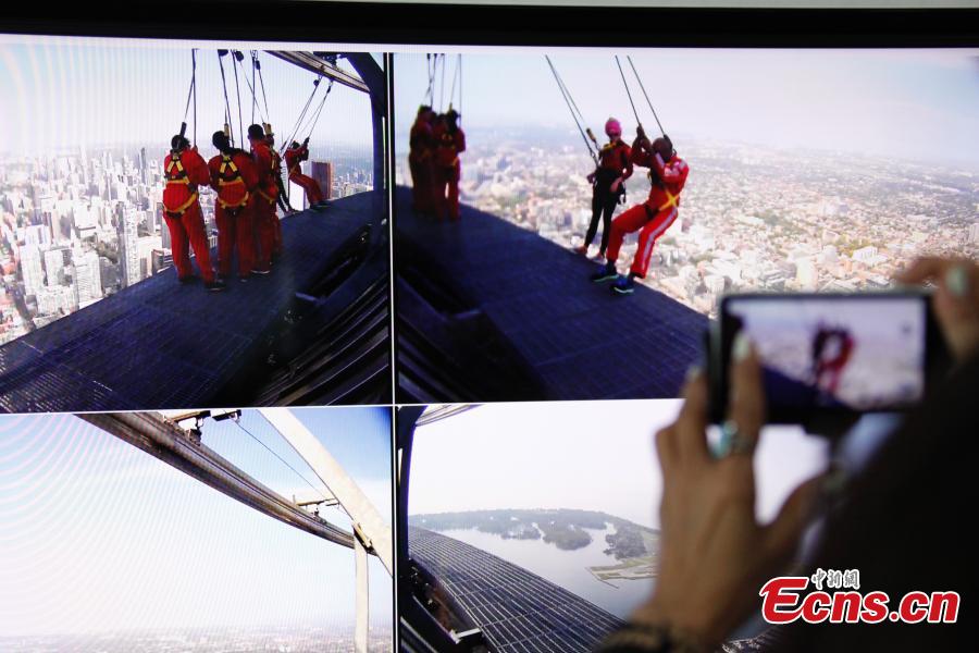 A relative takes photos of the live broadcast of six new Canadians who take their oath of citizenship while harnessed on the CN Tower\'s \