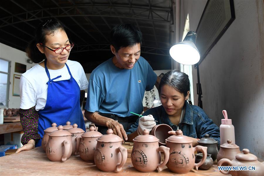 Zhang Chuanrui (C), an experienced Nixing pottery artisan, gives instructions to a staff member at a workshop in Qinzhou, south China\'s Guangxi Zhuang Autonomous Region, Oct. 9, 2018. The making of Nixing pottery is a well-preserved tradition in Qinzhou. In 2008, the techniques of making Nixing pottery were listed as one of China\'s state-level intangible cultural heritages. Currently, over 10,000 workers are engaged in the Nixing pottery industry in Qinzhou, producing more than 1,000 pottery varieties. (Xinhua/Lu Boan)