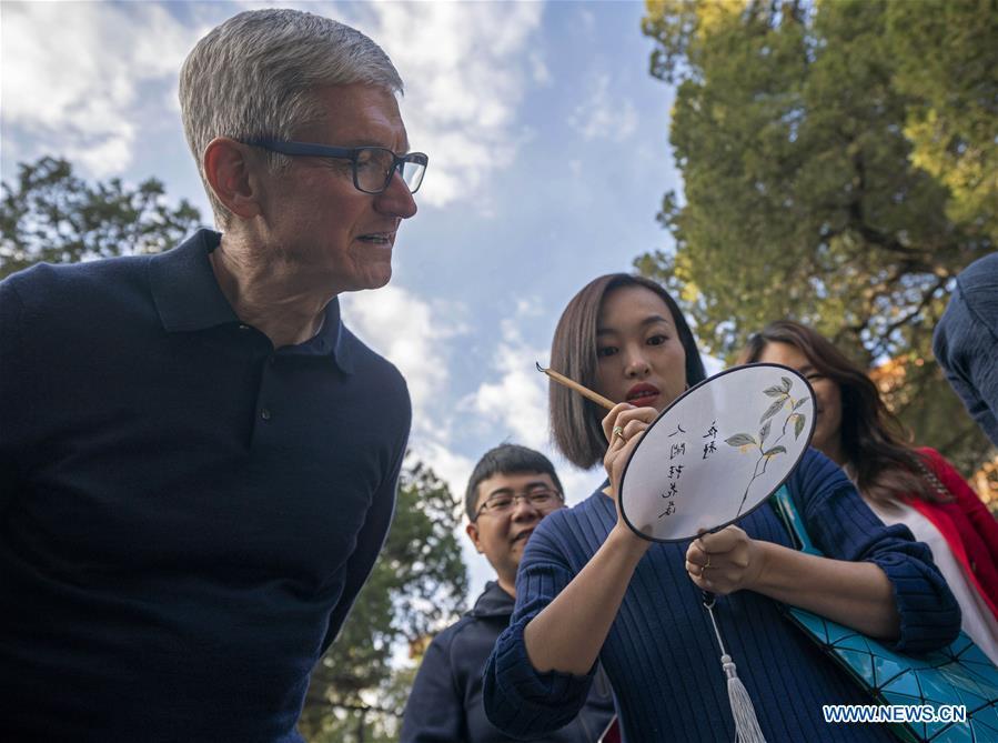 Apple\'s CEO Tim Cook looks at a woman writing calligraphy on a fan at Beijing Confucian Temple in Beijing, capital of China, on Oct. 10, 2018. Cook paid a visit to Beijing Confucian Temple and the Imperial College on Wednesday. (Xinhua/Cai Yang)