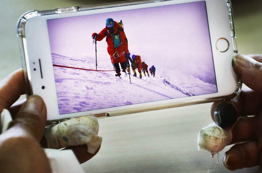 Xia looks at the photos and recalls the experience of climbing Qomolangma.(Photo/China Daily)
\