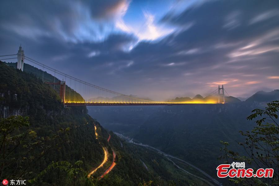 An early morning view of a winding road on a mountain and the Aizhai Bridge in Jishou City, Central China’s Hunan Province, Oct. 17, 2018. The suspension bridge was built as part of an expressway from southwest China\'s Chongqing Municipality to Changsha. The bridge links two tunnels 1,176 meters apart and carries traffic 330 meters above the floor of the Dehang Canyon, setting several records including the world\'s highest and longest tunnel-to-tunnel bridge. (Photo/IC)